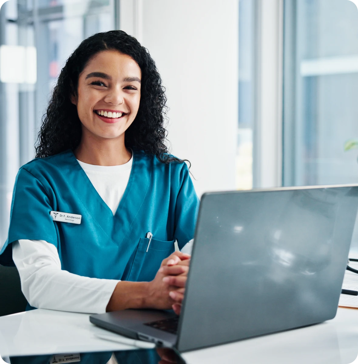 Woman in scrubs sitting at a desk with a laptop computer in front of her